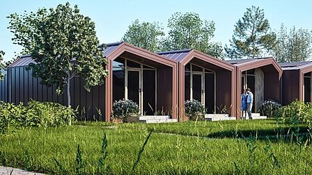 3 woonunits (containers met lazen wand aan het uiteinde) naast elkaar in een groene omgeving. 2 mensen staan voor een van de units