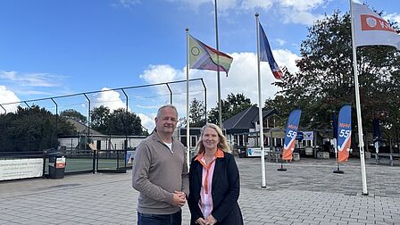 Karin van Vliet en voorzitter MHV schudden elkaar de hand voor een vlaggenstok met progressvlag