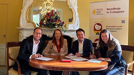 Bestuurslid, wethouder, voorzitter en secretaris zitten om een ronde tafel en tekenen de samenwerkingsovereenkomst.